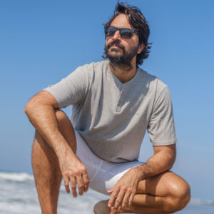 Man squatting on beach in Barra Cotton Tee Grey